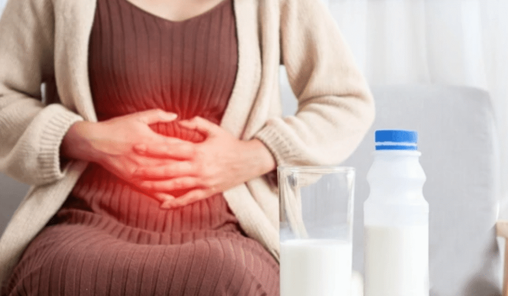 Woman experiencing lactose intolerance stomachache holding belly with milk glass and bottle nearby