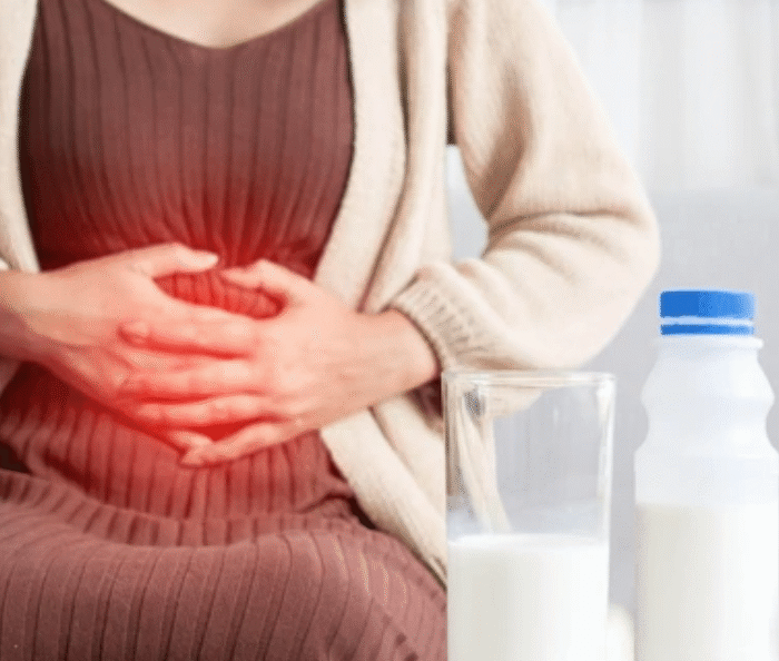 Woman experiencing lactose intolerance stomachache holding belly with milk glass and bottle nearby