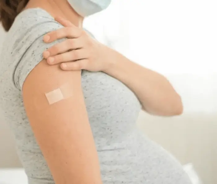 Pregnant woman wearing a mask after vaccination, supporting postpartum recovery and health after birth.