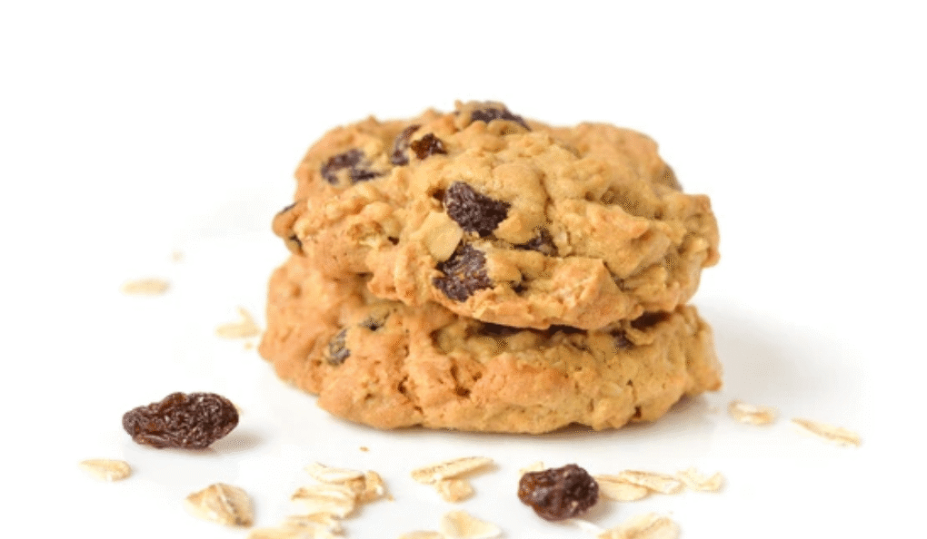 Stack of homemade oatmeal raisin cookies with scattered oats and raisins on white background