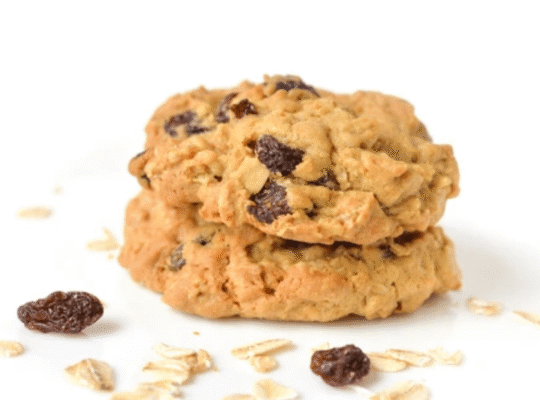 Stack of homemade oatmeal raisin cookies with scattered oats and raisins on white background