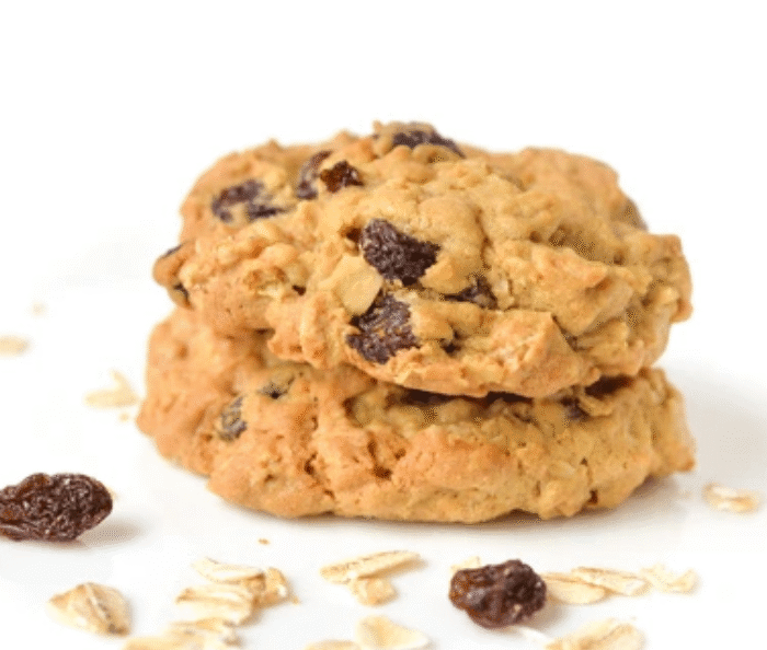 Stack of homemade oatmeal raisin cookies with scattered oats and raisins on white background