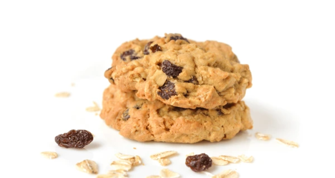 Stack of homemade oatmeal raisin cookies with scattered oats and raisins on white background