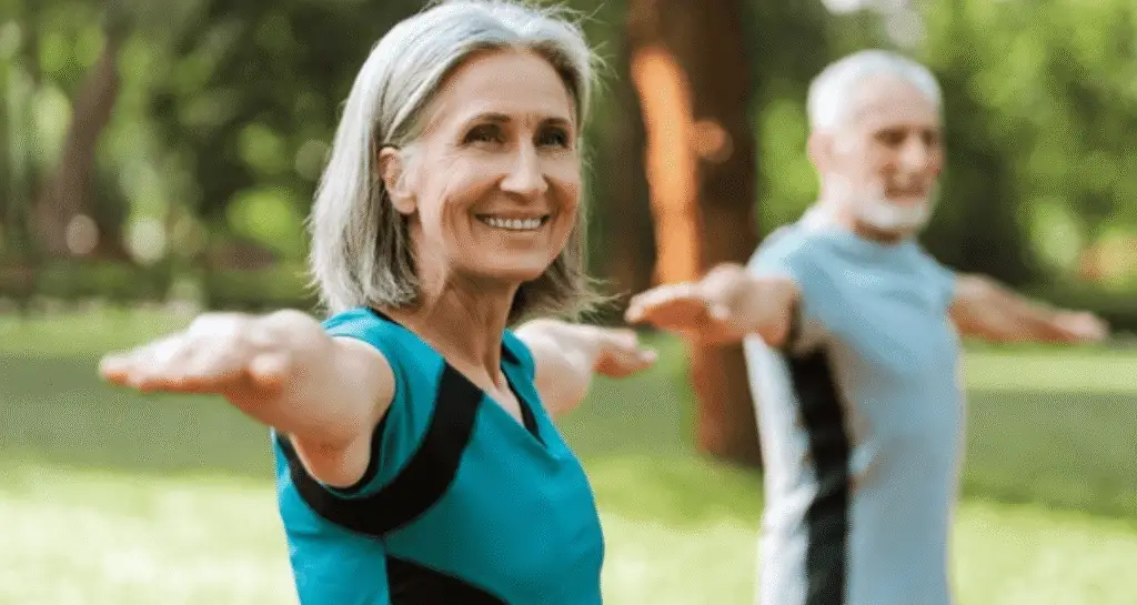 Senior woman practicing yoga energy poses outdoors to restore balance with partner in peaceful park setting