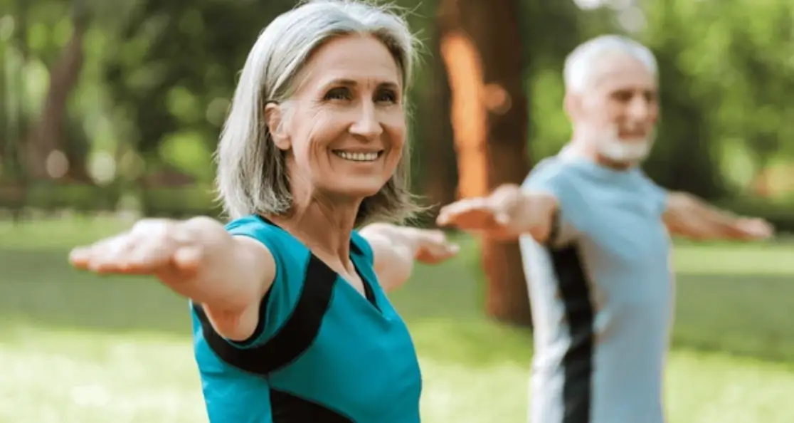 Senior woman practicing yoga energy poses outdoors to restore balance with partner in peaceful park setting