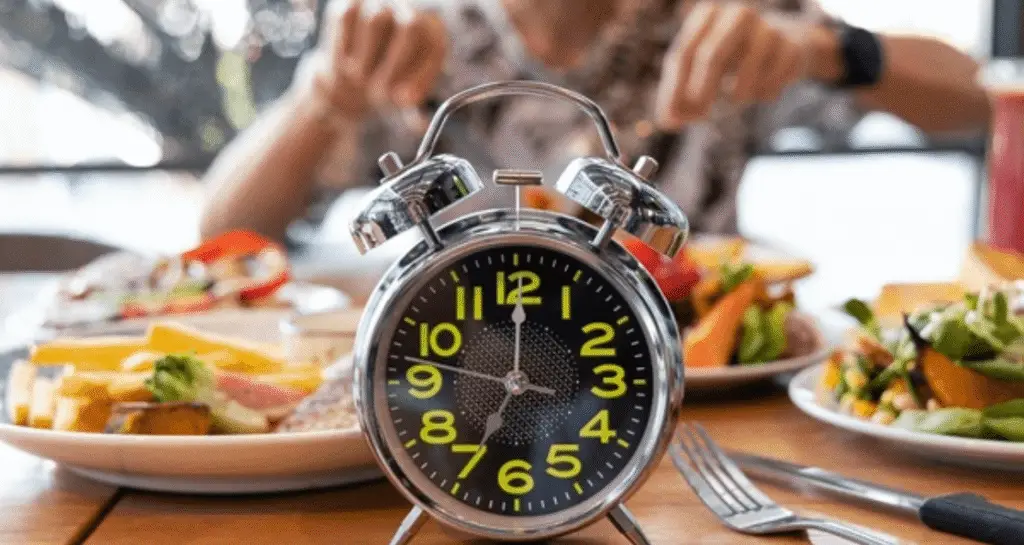 Vintage alarm clock showing meal timing next to healthy plates of food representing intermittent fasting vs calorie restriction eating schedules