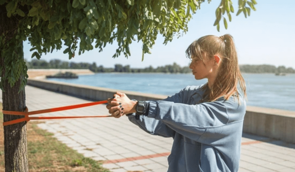Woman performing resistance band exercises muscle atrophy recovery outdoors by waterfront