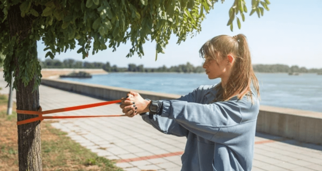 Woman performing resistance band exercises muscle atrophy recovery outdoors by waterfront
