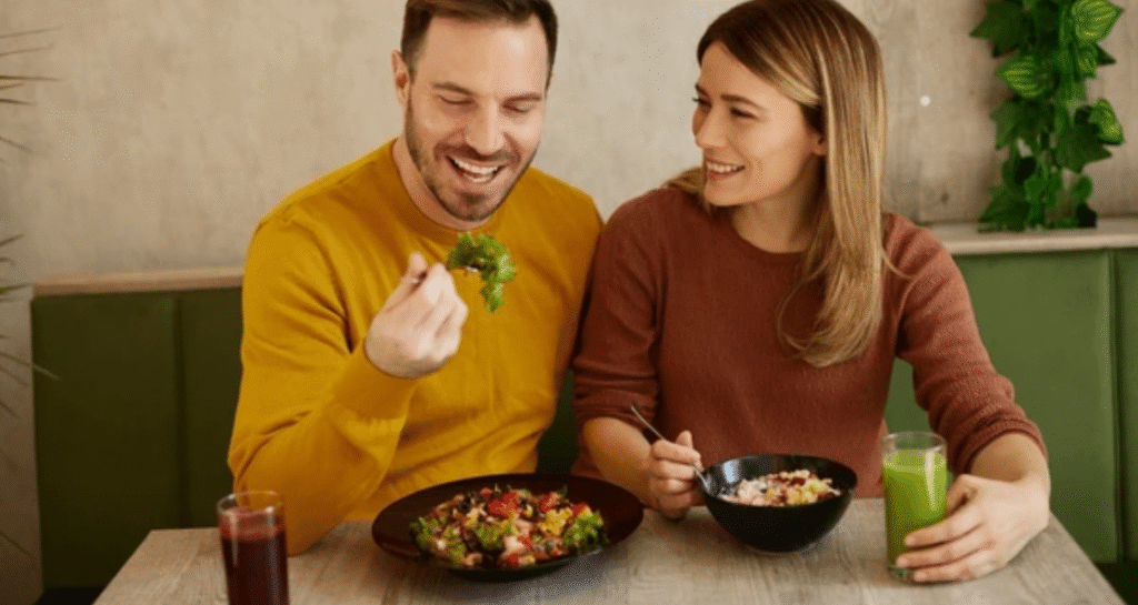 Happy couple eating healthy salads and drinking green smoothie at restaurant table
