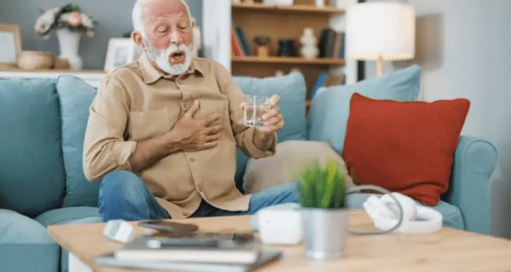 An elderly man experiencing chest pain and shortness of breath while holding his chest and a glass of water, highlighting concerns for his heart health.