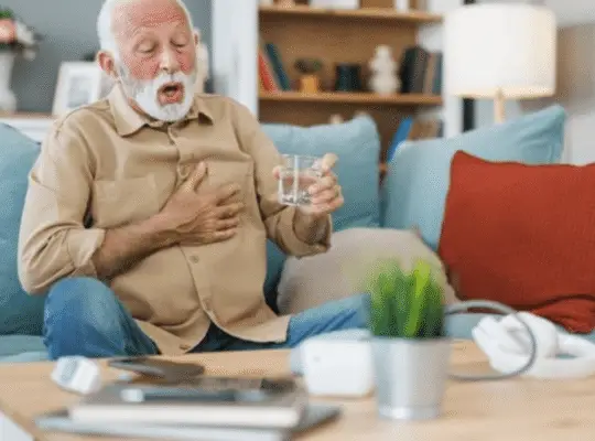 An elderly man experiencing chest pain and shortness of breath while holding his chest and a glass of water, highlighting concerns for his heart health.