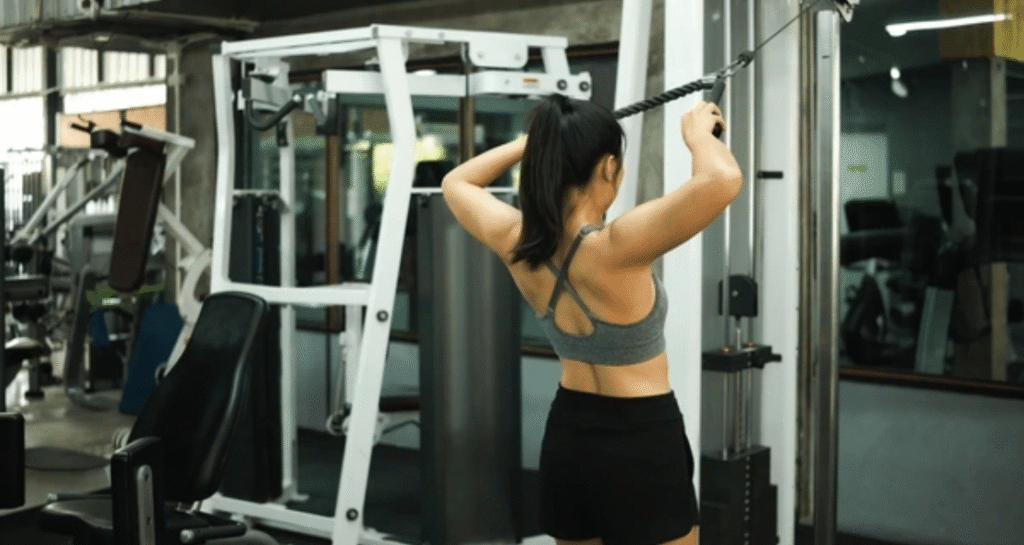 Woman performing face pulls exercise for shoulders at cable machine in gym