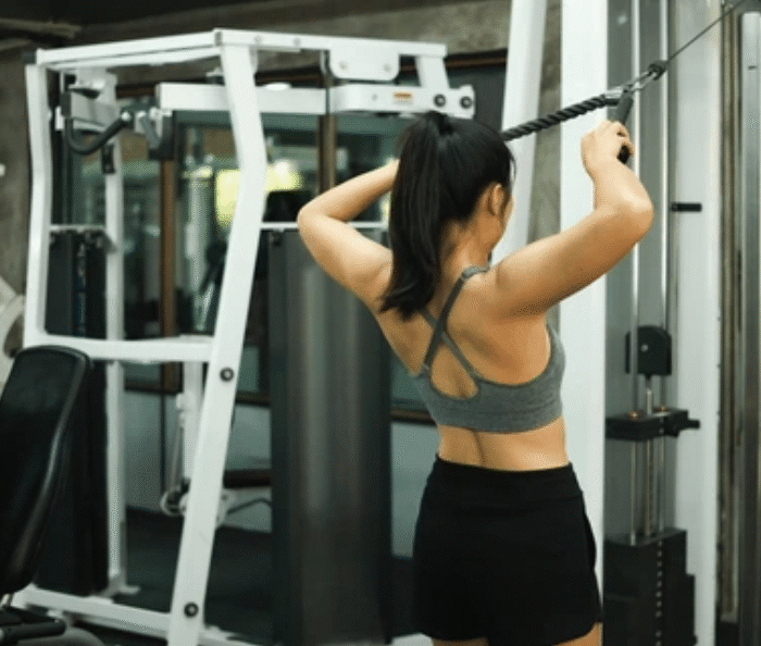 Woman performing face pulls exercise for shoulders at cable machine in gym