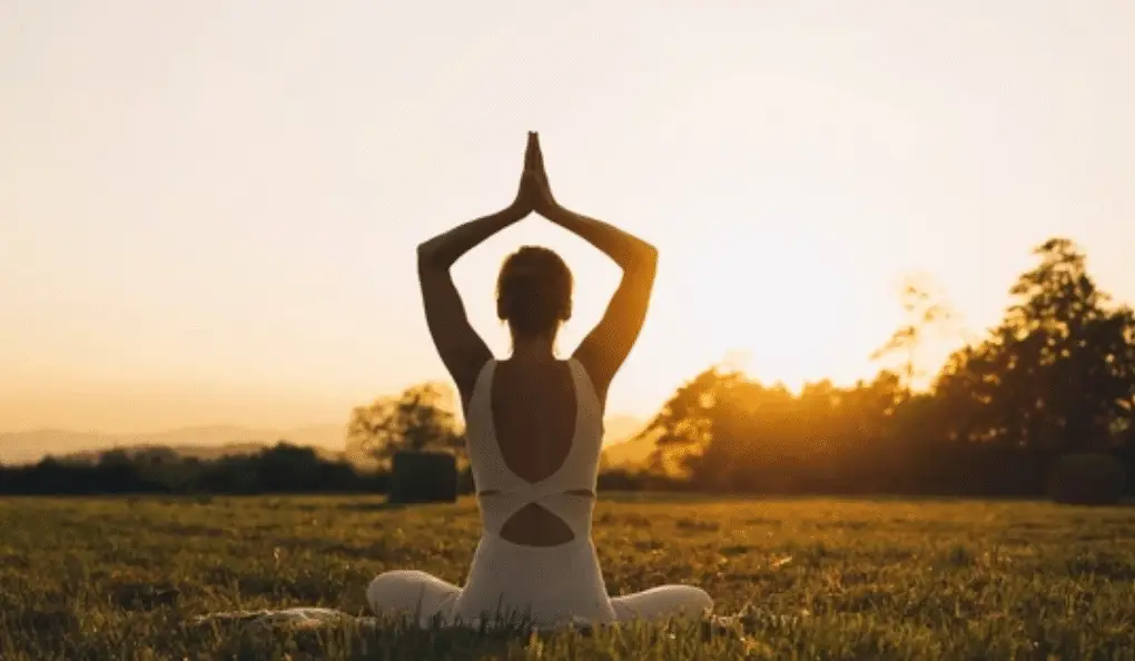 Woman practicing yoga energy restore pose at sunset in peaceful field setting