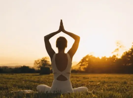 Woman practicing yoga energy restore pose at sunset in peaceful field setting