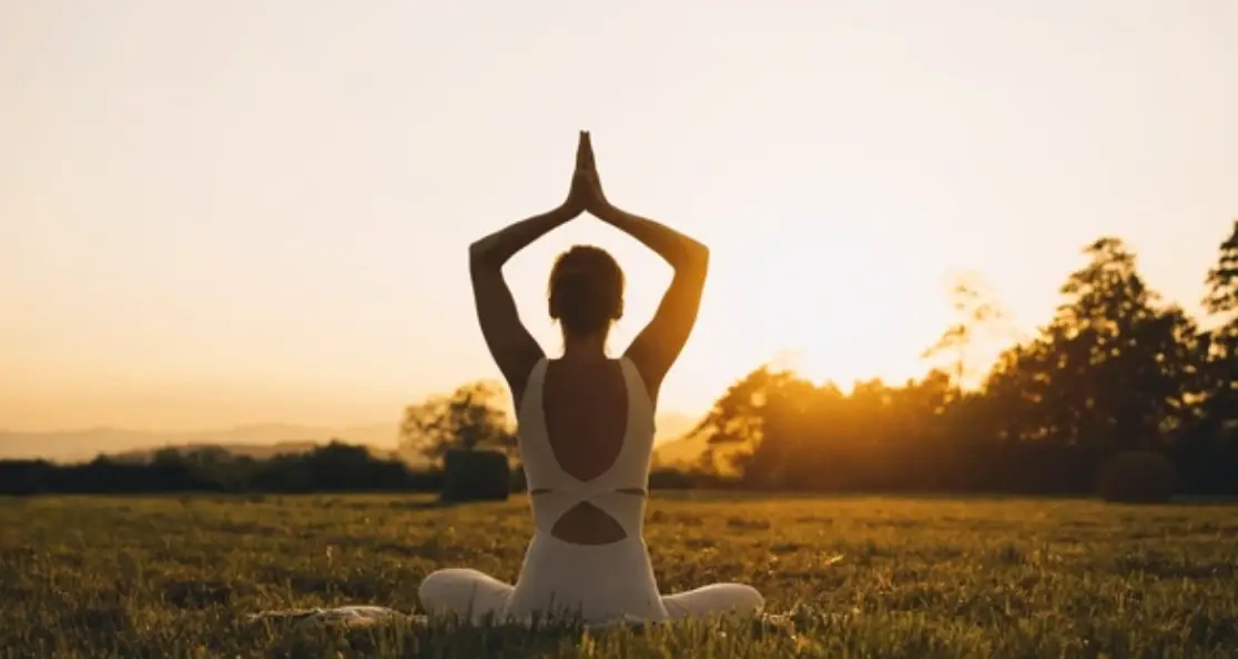 Woman practicing yoga energy restore pose at sunset in peaceful field setting