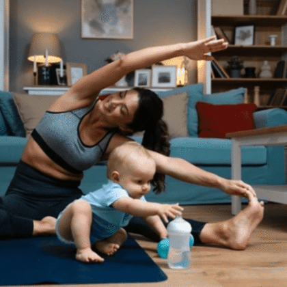 Woman doing postpartum yoga stretches with baby on exercise mat - postpartum weight loss tips for women